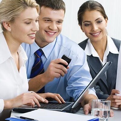 Three people are sitting at a table and one is using his laptop.